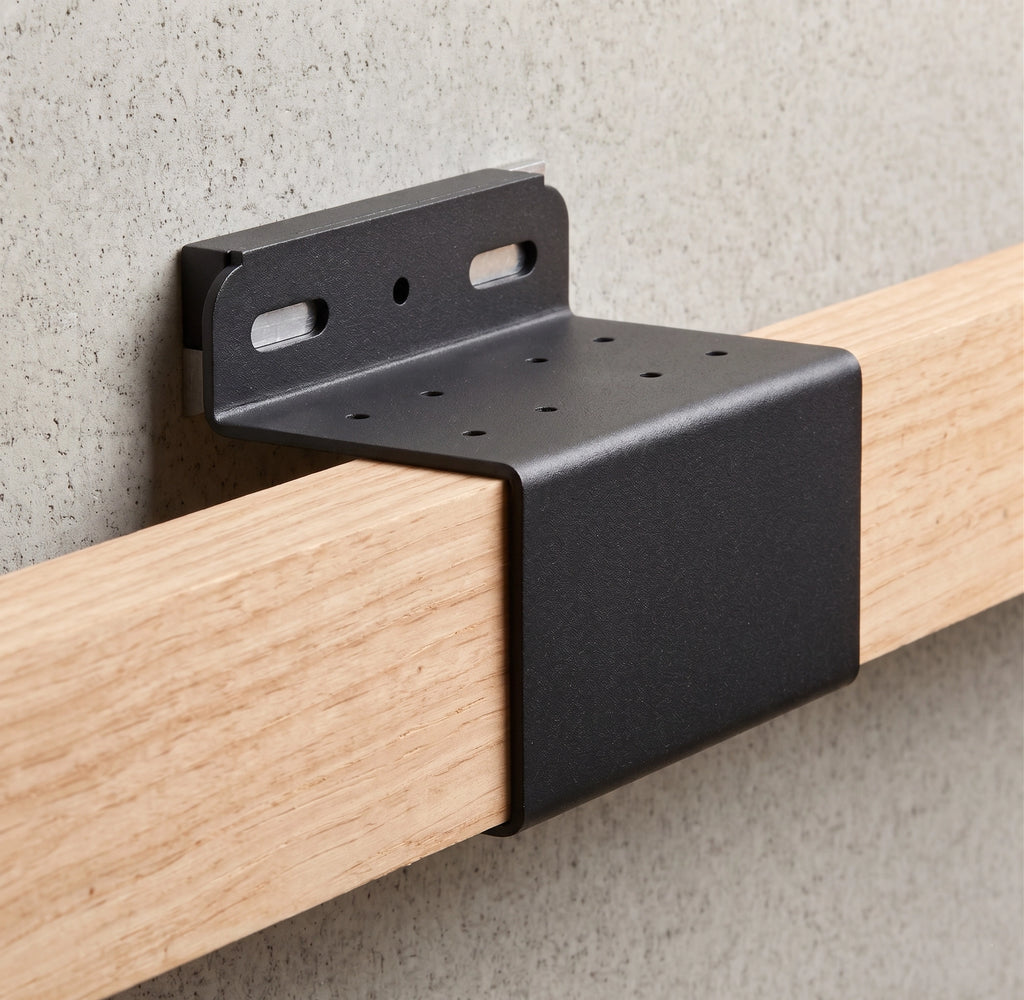 Black metal bracket attached to a wooden rod against a gray concrete wall.