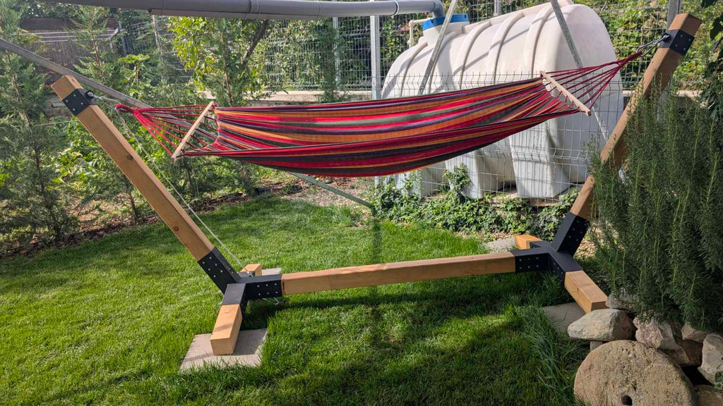 Red and brown striped hammock on a wooden stand in a garden setting